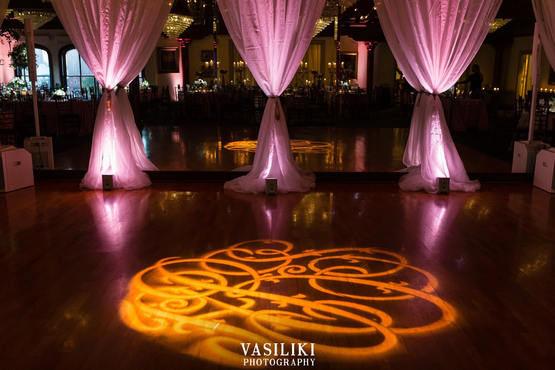 A dance floor with a lit monogram between draped columns